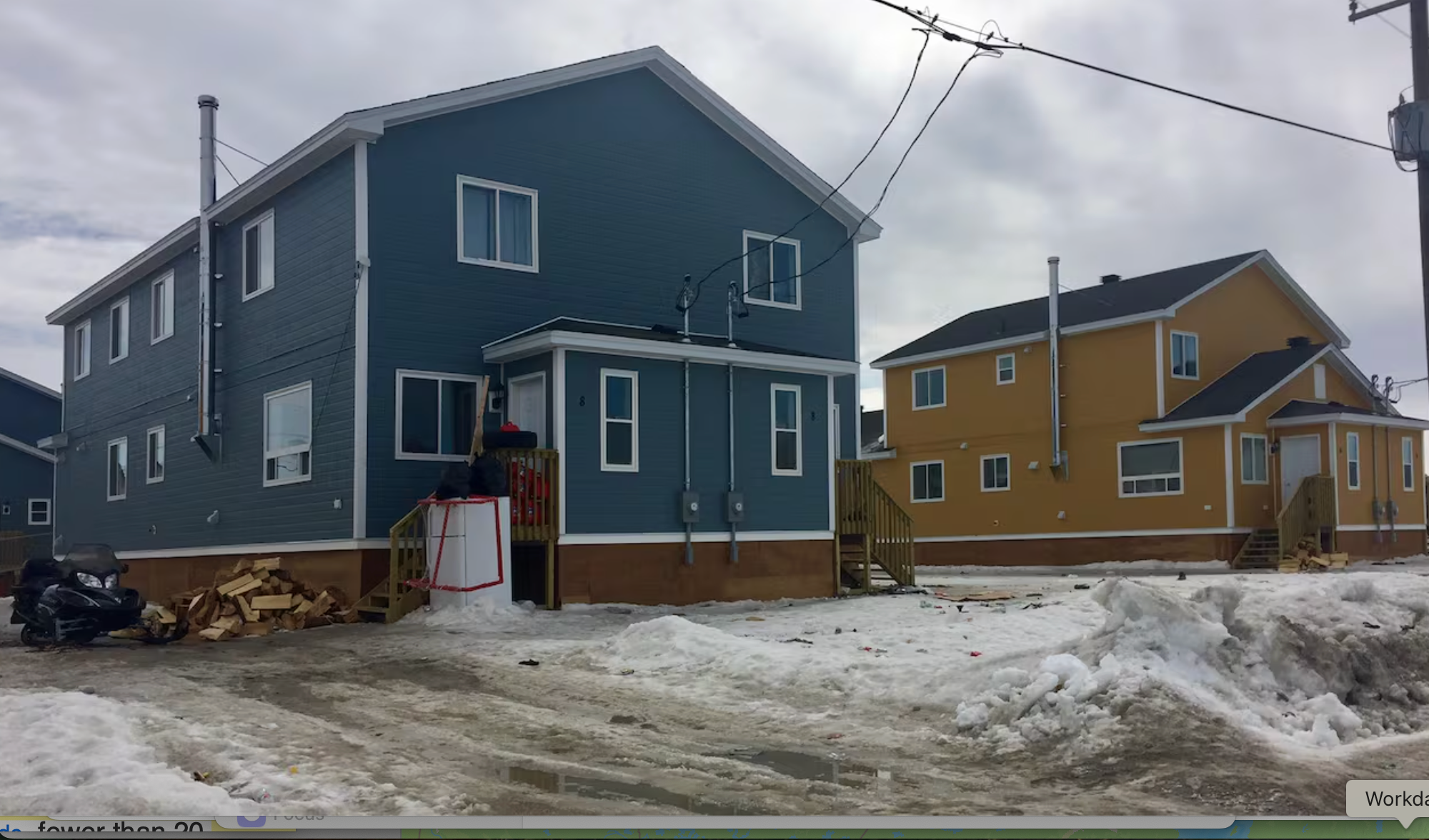A two-storey blue house is next to a yellow one on snowy ground. 